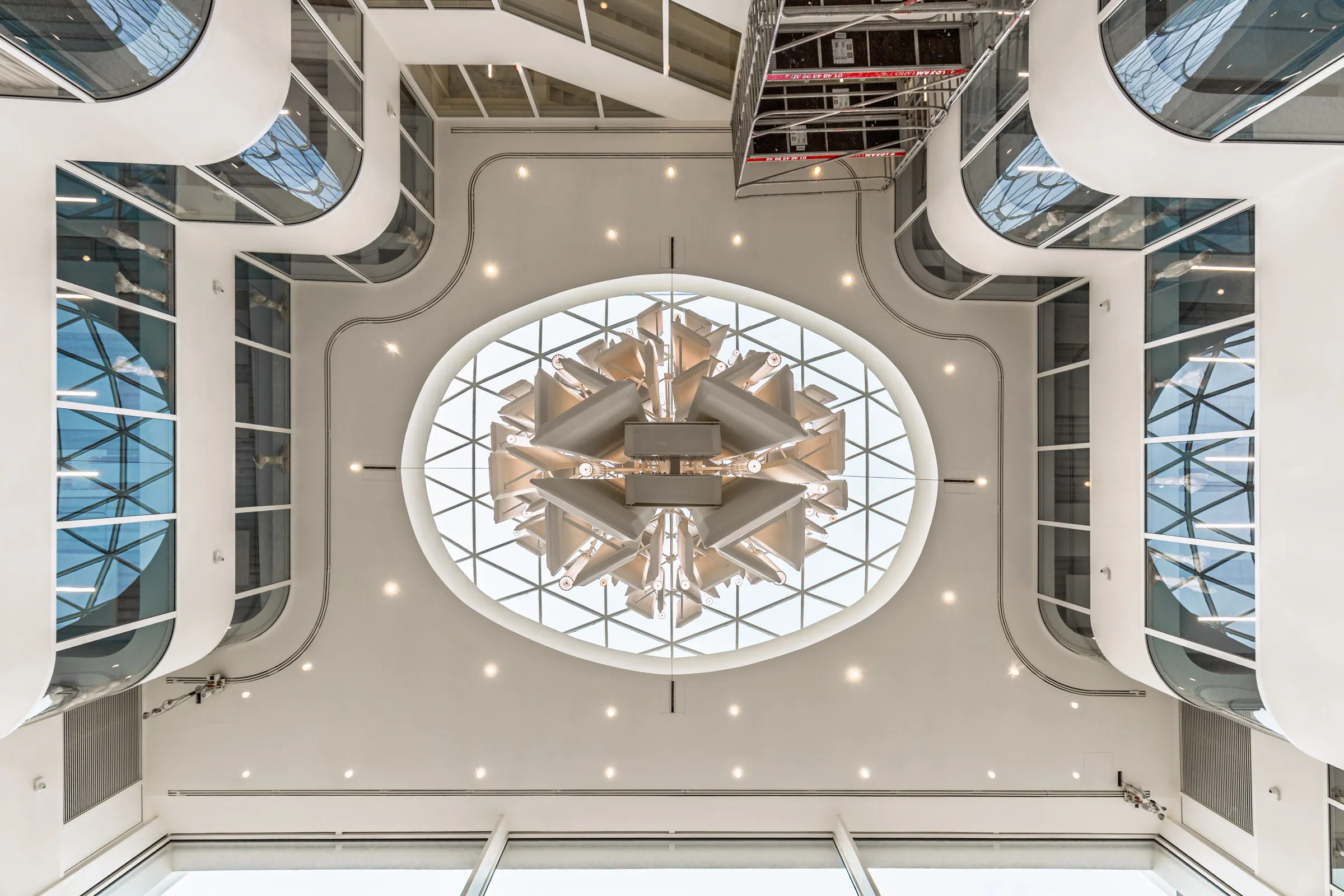 Vue ascendante vers la verrière ovale et le luminaire au coeur de l’atrium
