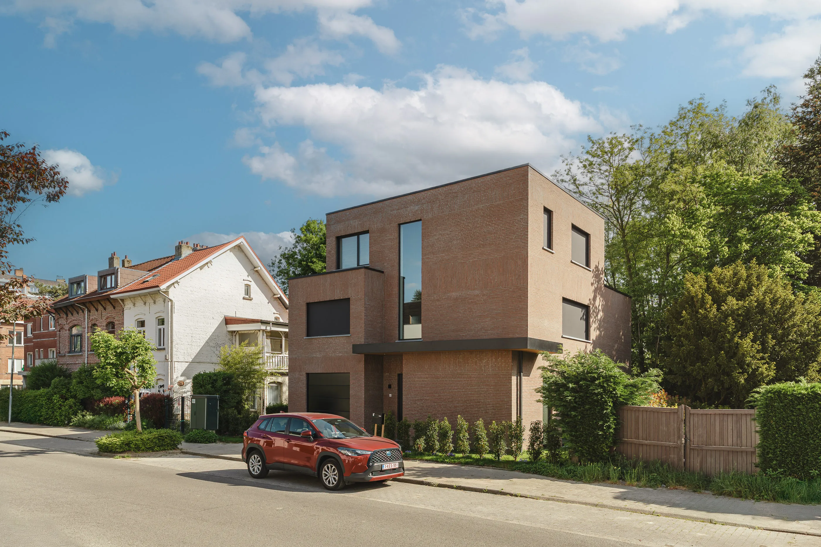 Vue depuis la rue de la maison en brique, près de maisons anciennes à toiture inclinée et d’arbres adultes