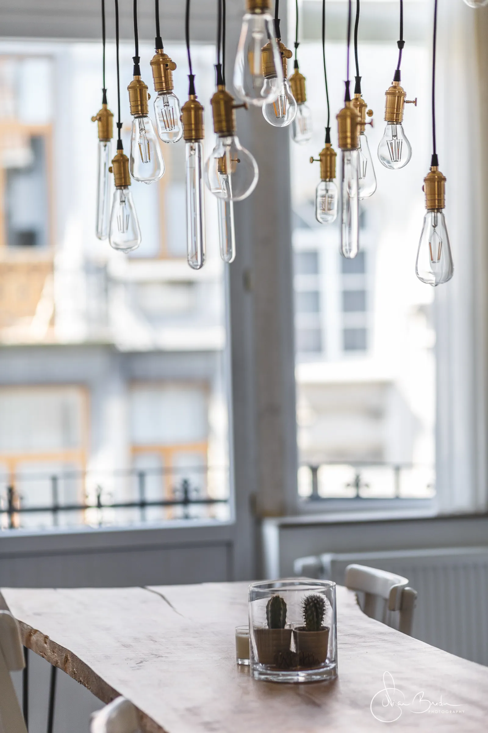 Dining table and hanging lights set before tall windows and a white kitchen