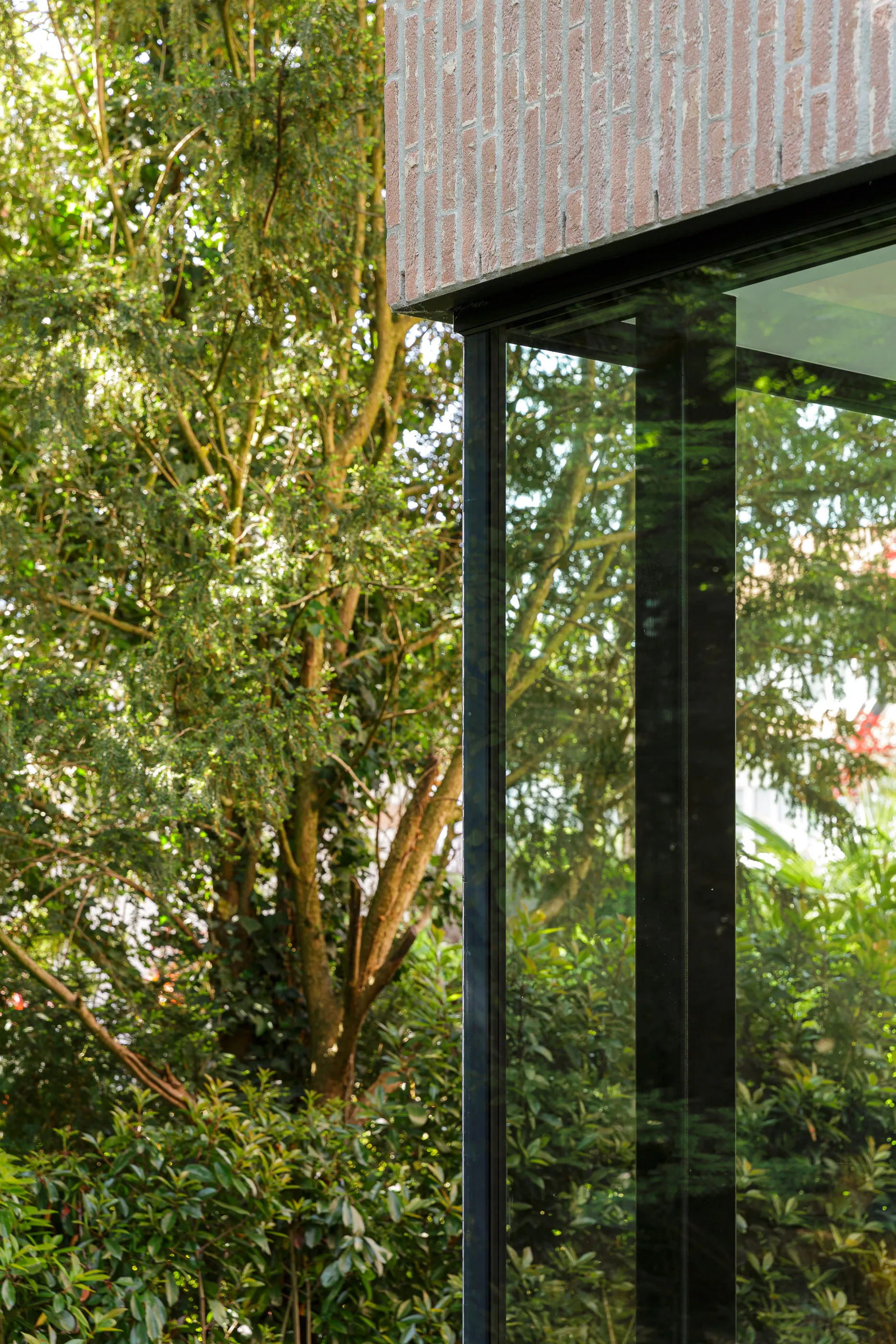 Angle vitré reflétant la végétation dense du jardin sous un porte-à-faux en brique