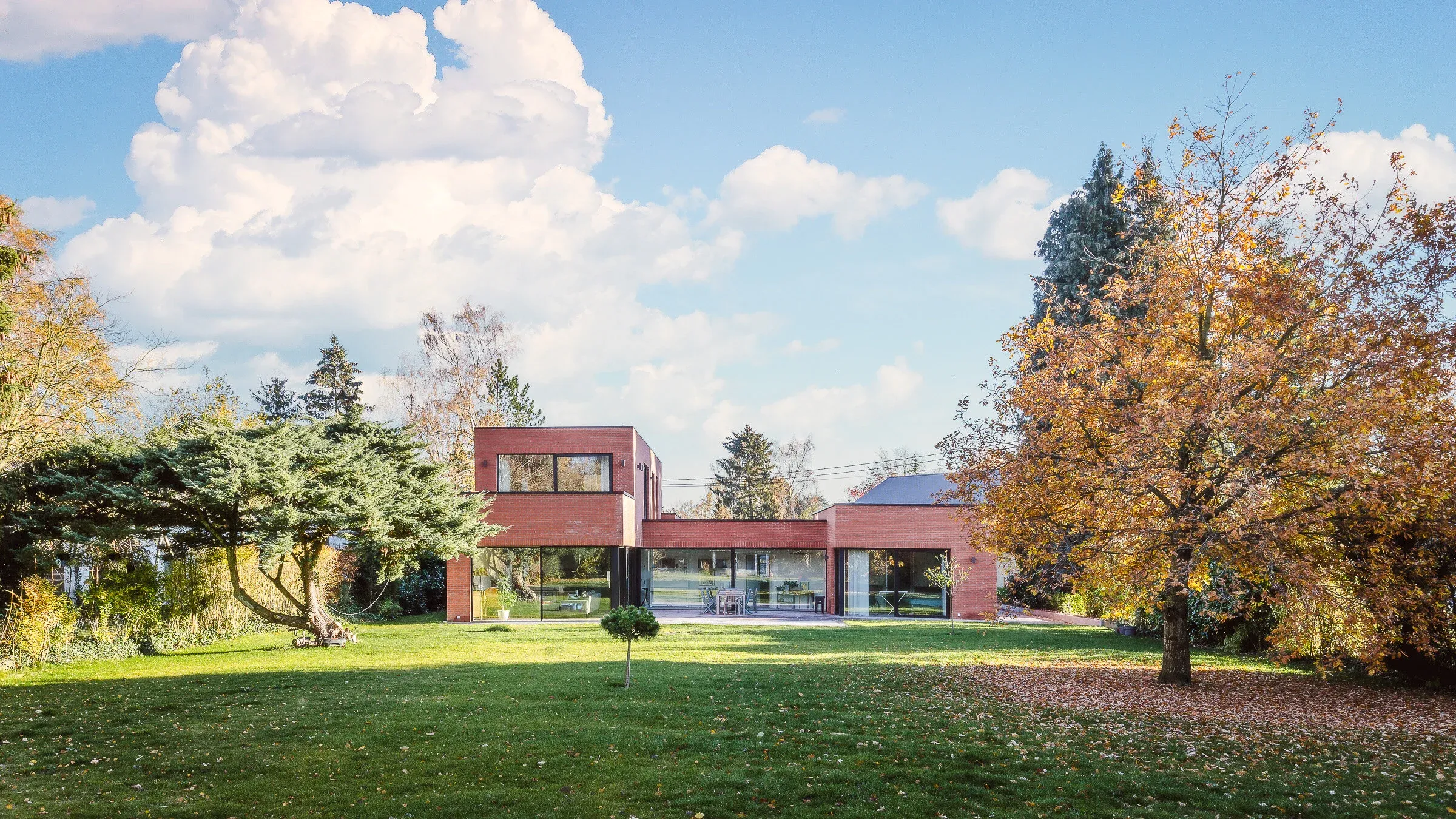 Vue large depuis le jardin sur la maison basse en brique rouge sous les arbres d’automne
