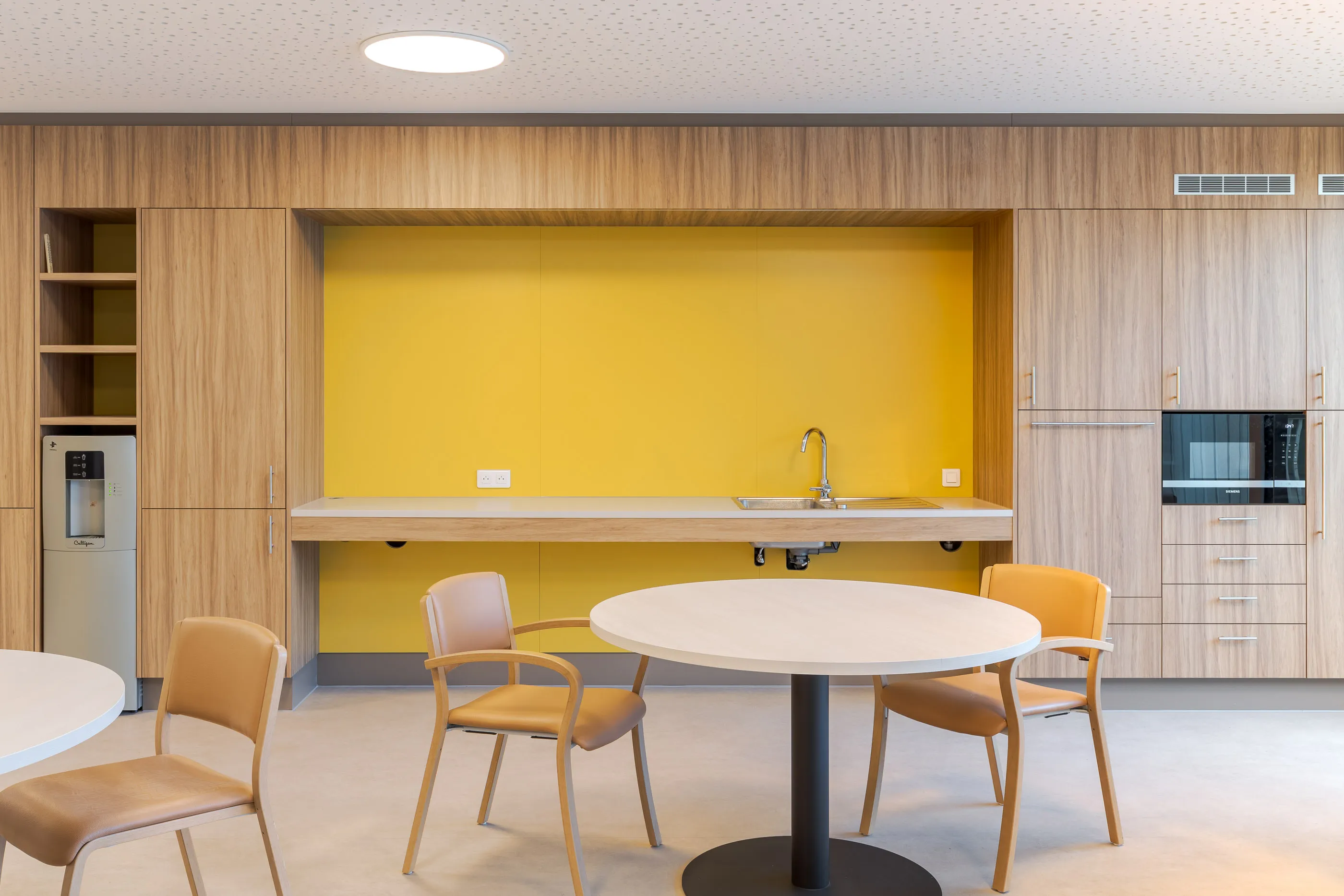Salle à manger avec tables rondes, rangements en bois et niche de cuisine jaune vif