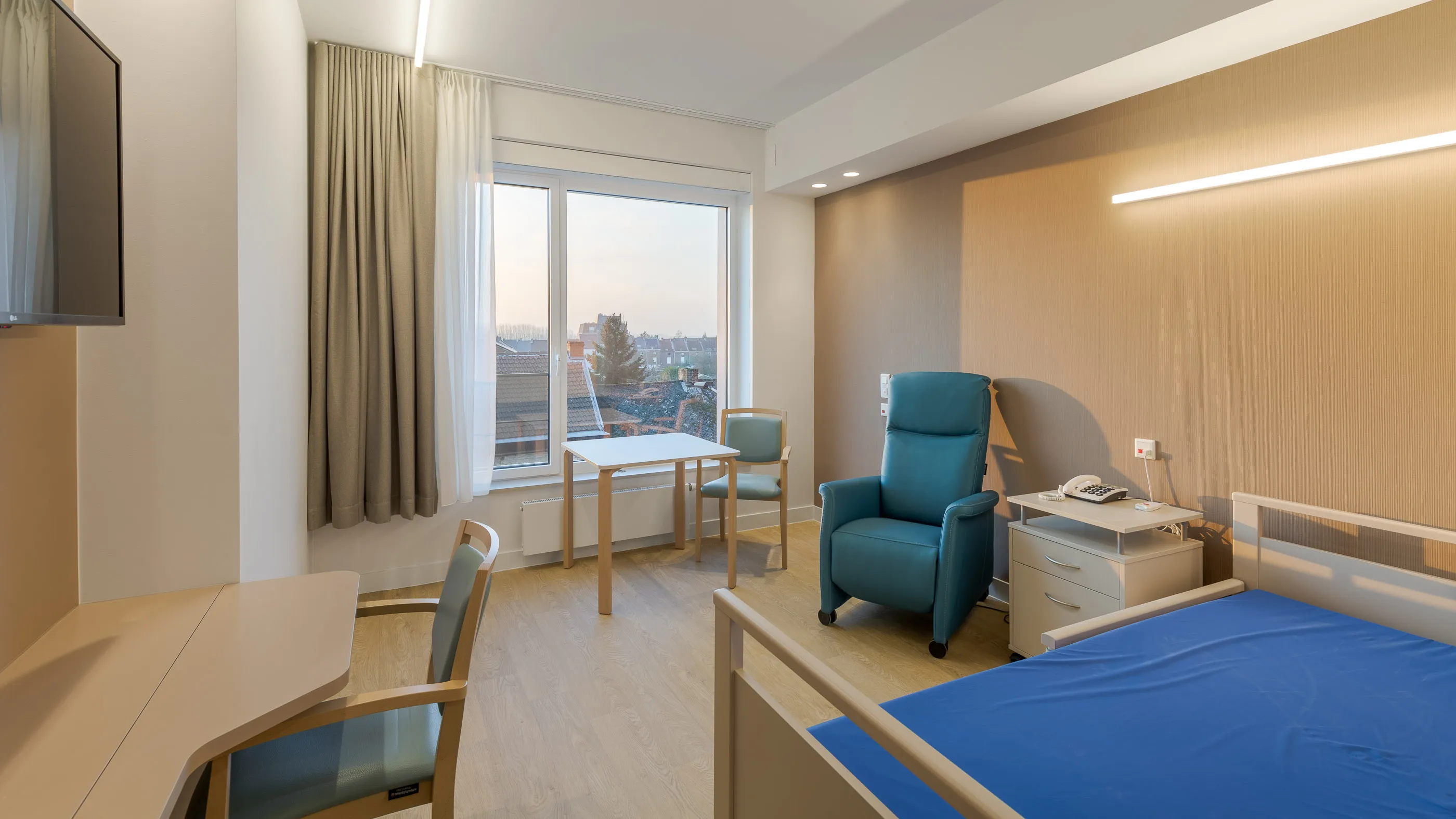 Chambre avec couvre-lit bleu et fauteuil inclinable éclairés par le soleil bas