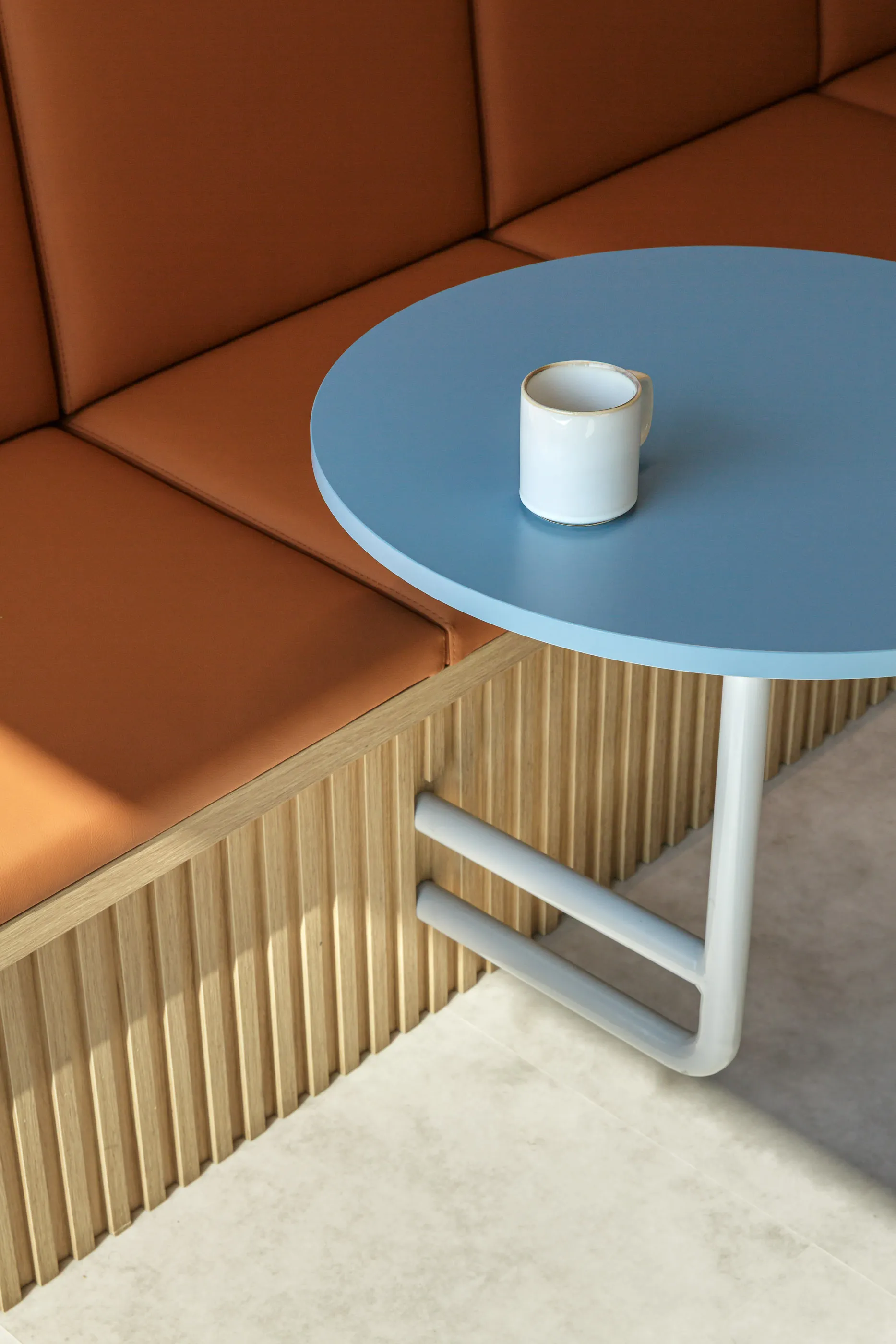 Tasse blanche sur une table ronde bleue, près d’une banquette capitonnée couleur rouille