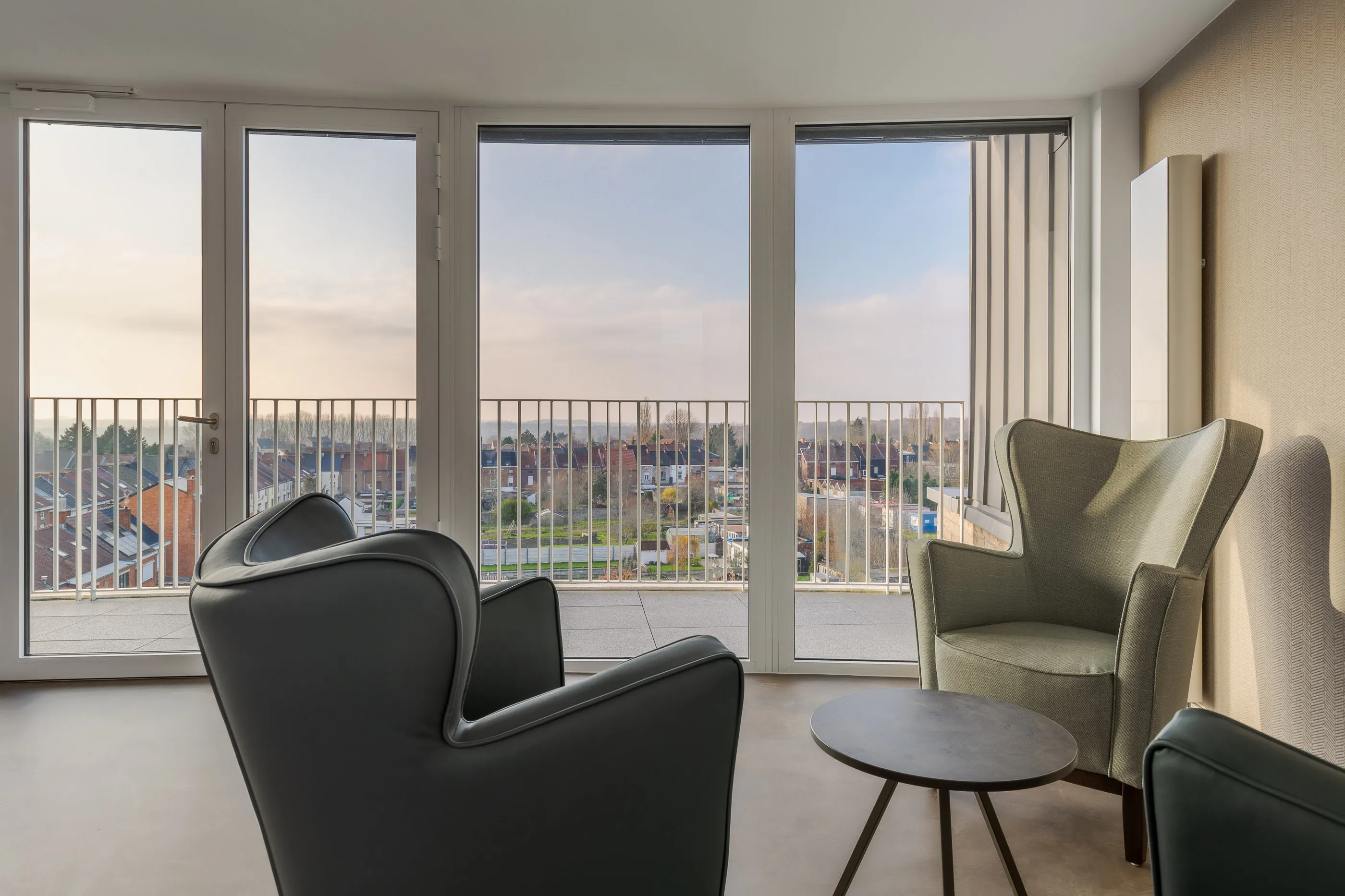 Trois fauteuils tournés vers des baies toute hauteur et une terrasse dominant le quartier