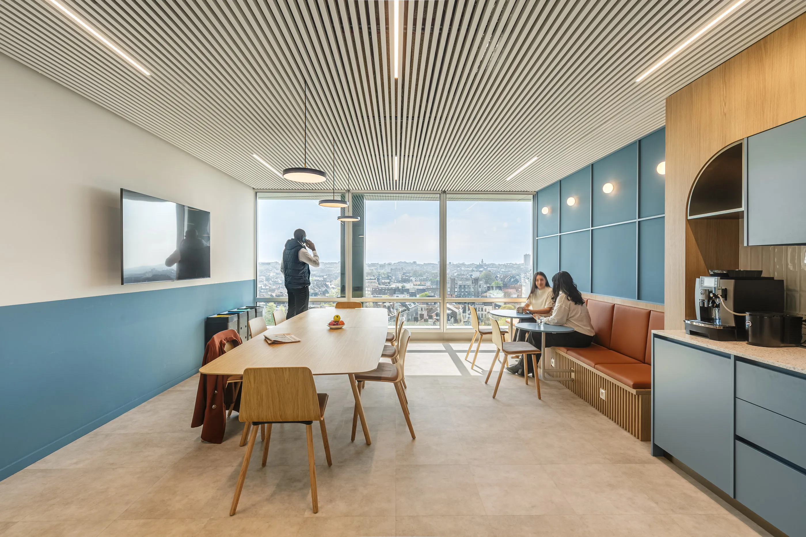 Cuisine et salle à manger partagées avec rangements bleus, table en bois et vue sur la ville