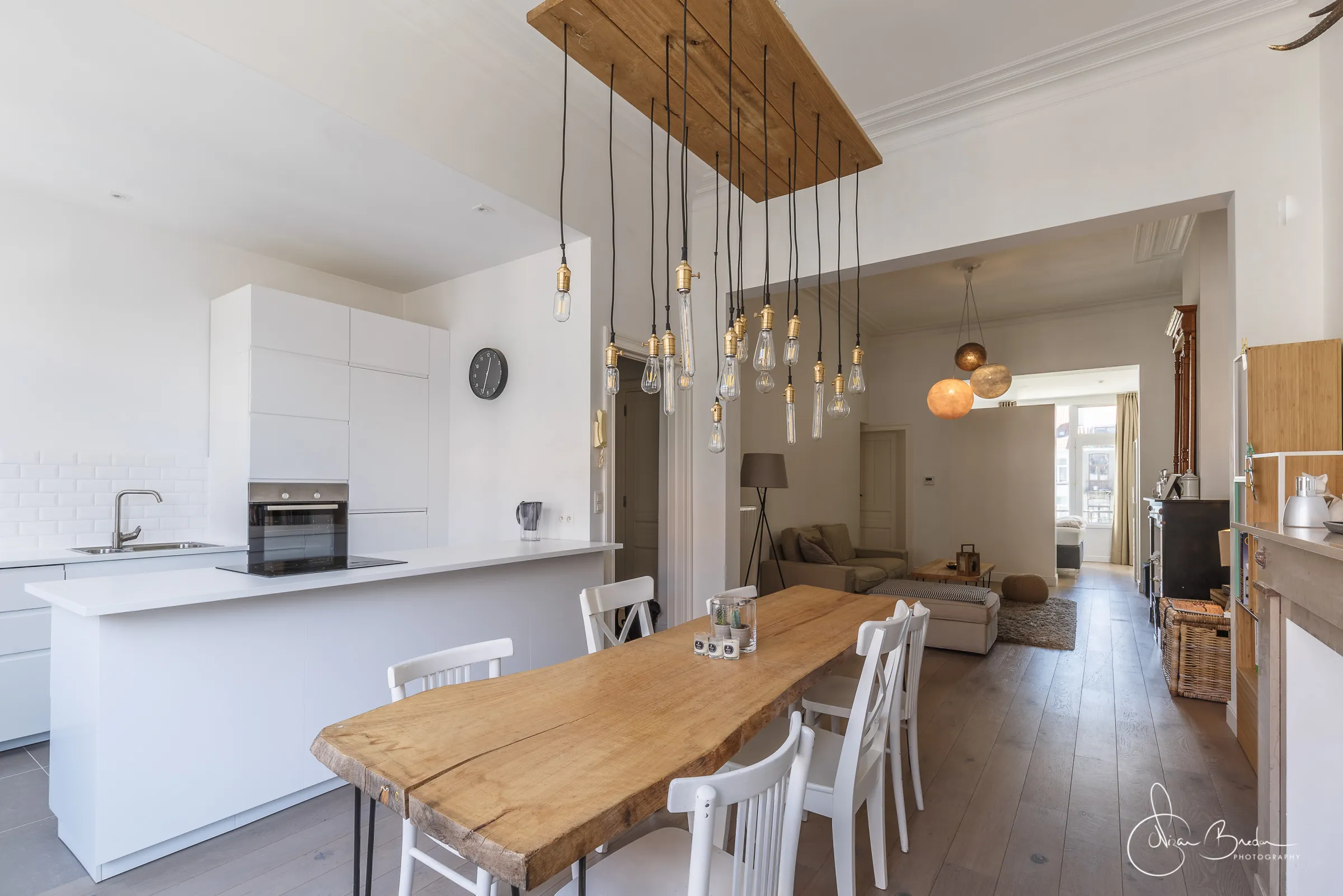White kitchen, long timber table and living room united by a field of pendant lights
