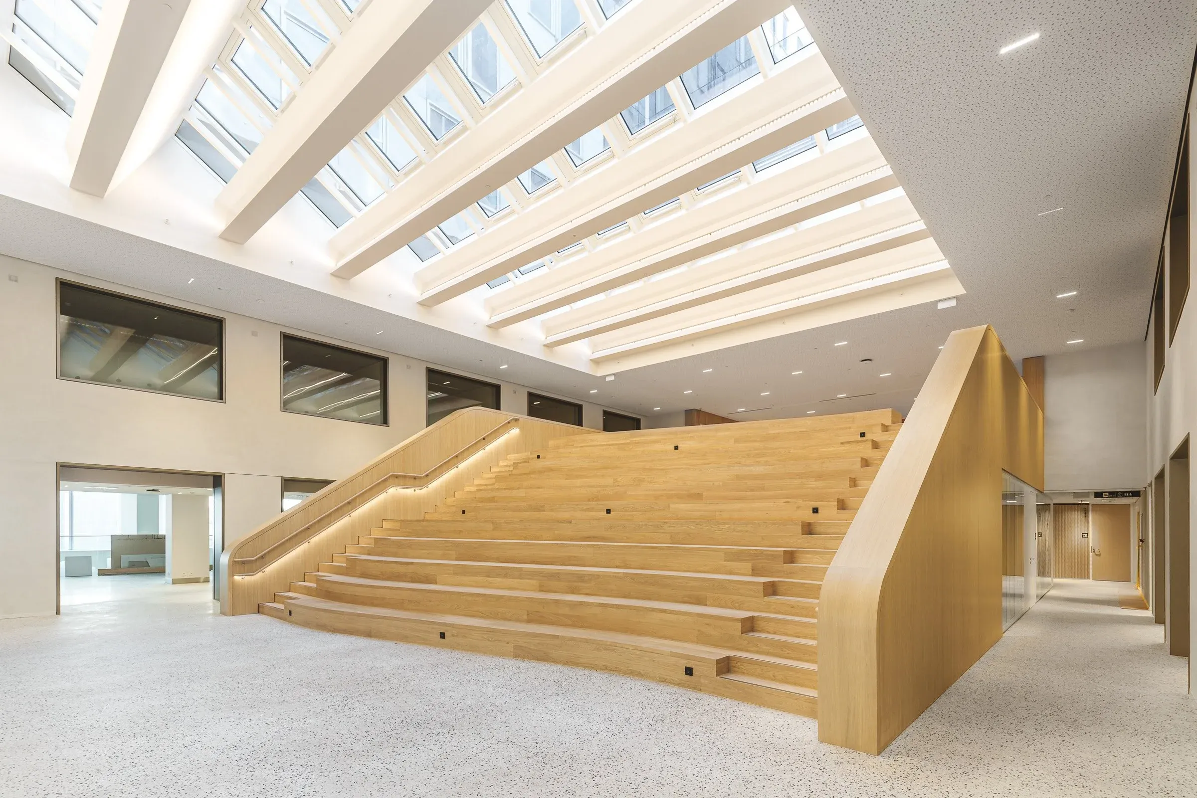 Vue large de l’agora éclairée en toiture et de ses gradins en bois