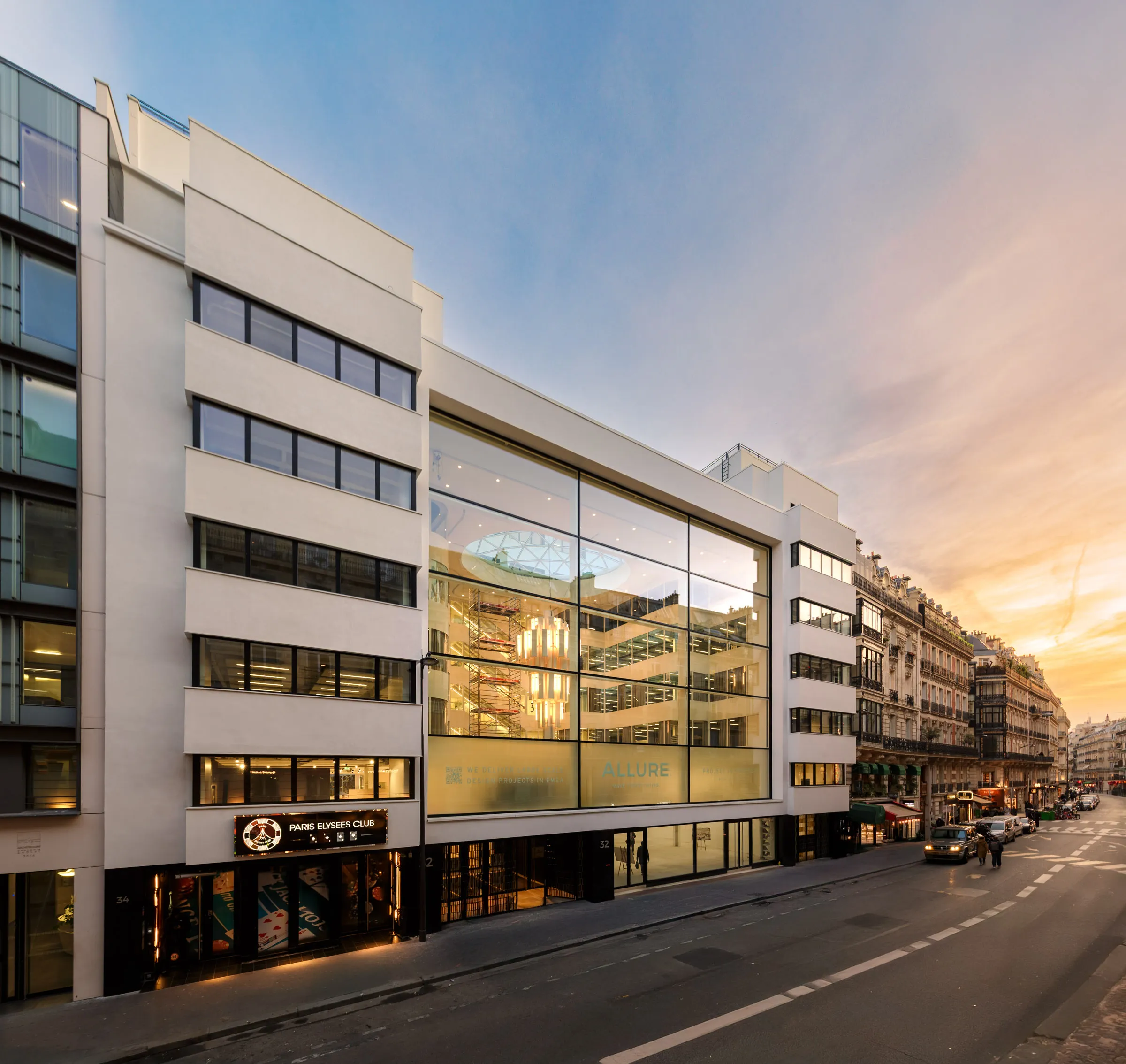 Icône vue depuis la rue Marbeuf au crépuscule, avec l’atrium vitré éclairé de l’intérieur