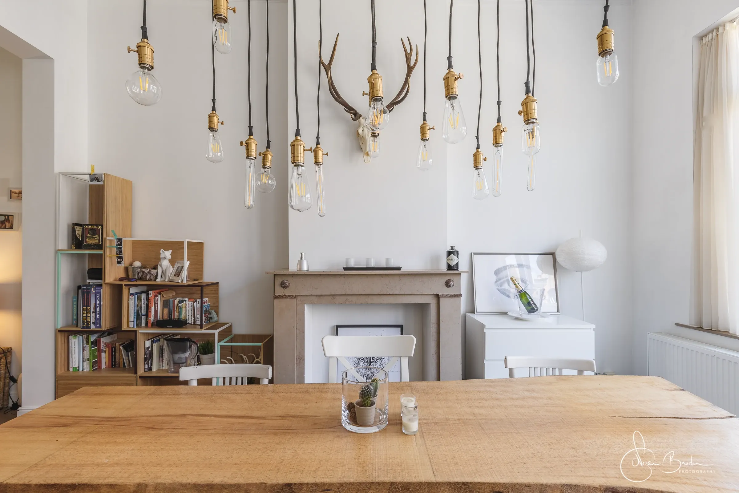 Hanging filament bulbs above a timber dining table and stone fireplace