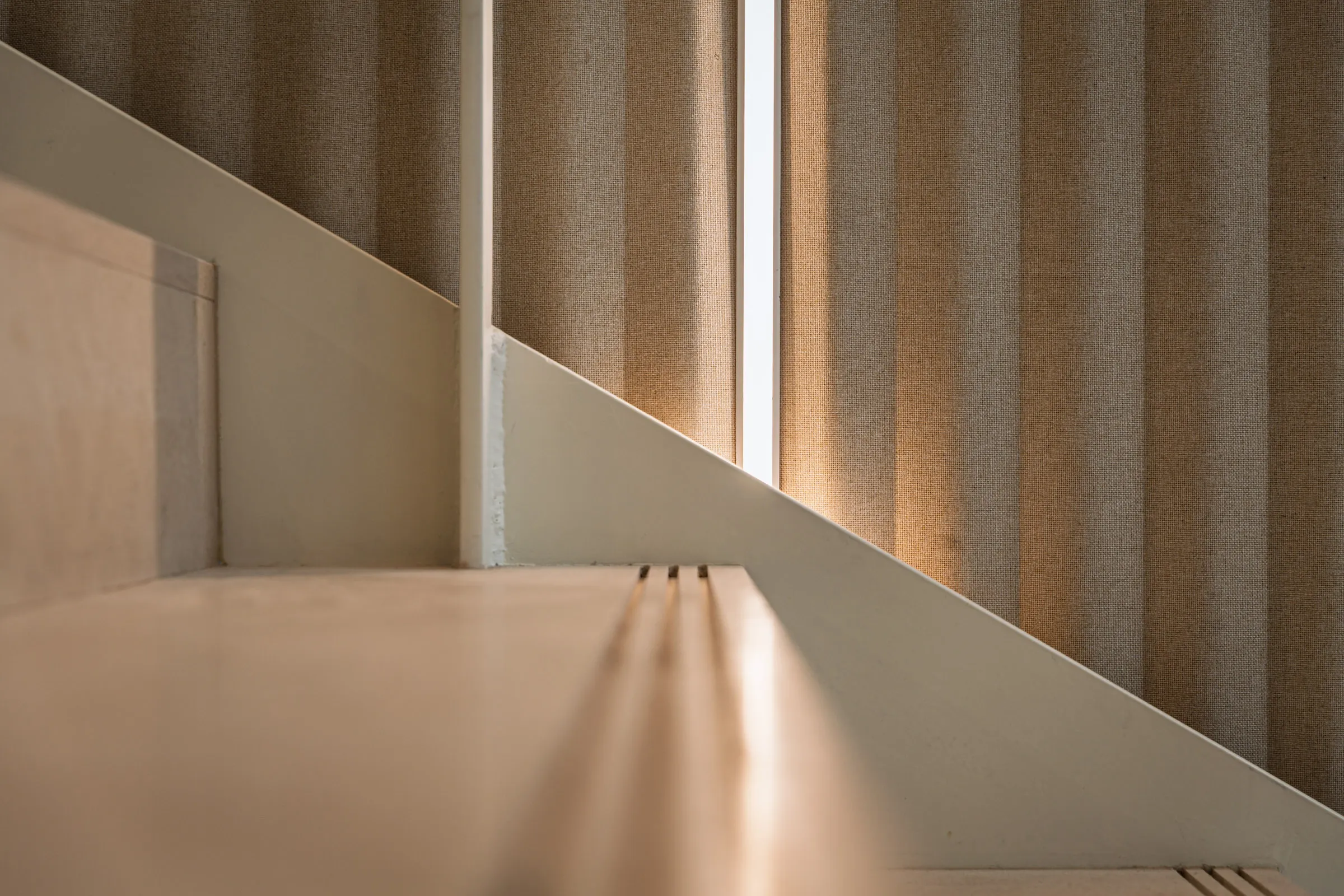 Jonction entre escalier et paroi textile dans une lumière chaude de fin de journée