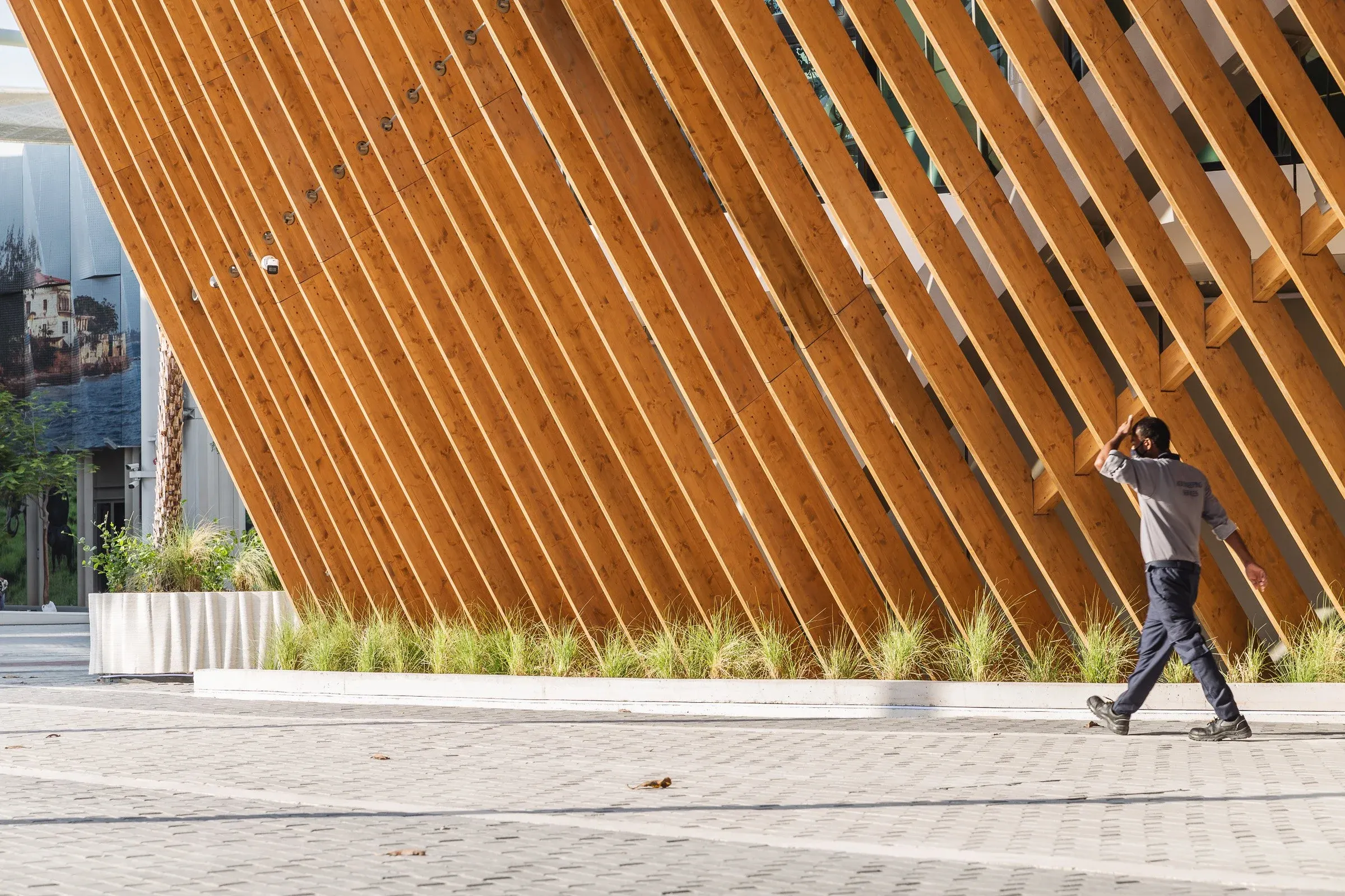 Visiteur longeant les lames verticales en bois du pavillon